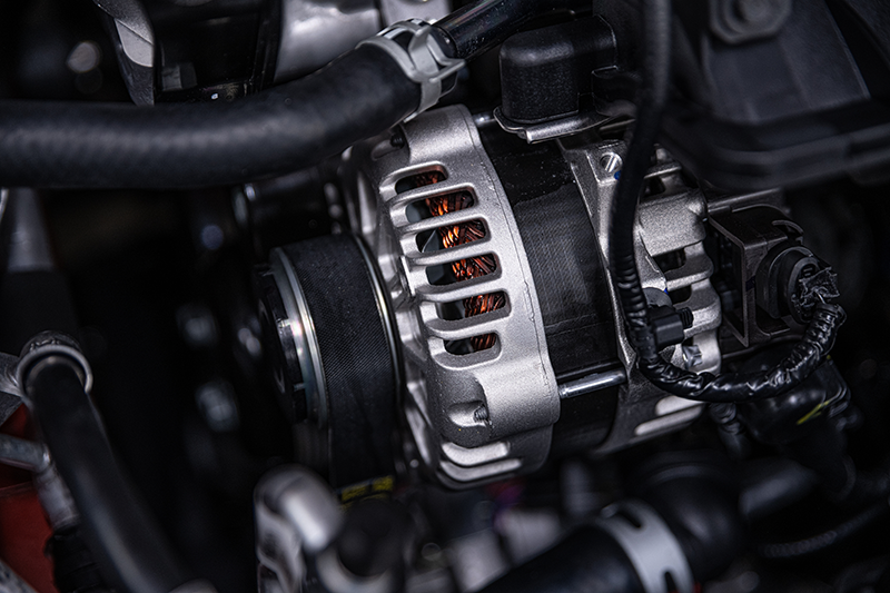 Close-up of a car alternator, showing the silver housing, black pulley, and copper coils within the engine bay.